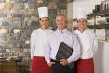 Photo: Restaurant manager standing with male and female chefs near commercial kitchen, smiling, front view, portrait Restaurant manager standing with male and female chefs near commercial kitchen, smiling, front view, portrait
