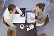 Photo: Couple sitting face to face at café table, man writing in folder, woman using laptop, smiling, side view, overhead view Couple sitting face to face at café table, man writing in folder, woman using laptop, smiling, side view, overhead view