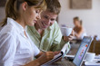 Photo: Couple sitting at café table with laptop, woman writing in notepad, man drinking cup of coffee, smiling, side view Couple sitting at café table with laptop, woman writing in notepad, man drinking cup of coffee, smiling, side view