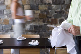 Photo: Waiter and waitress laying tables in restaurant, focus on man wiping knife in foreground, side view (blurred motion) Waiter and waitress laying tables in restaurant, focus on man wiping knife in foreground, side view (blurred motion)