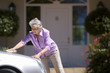 Senior woman polishing silver car parked on driveway in front of house, smiling, side view