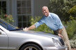 Senior man polishing silver car parked on driveway in front of house, smiling, side view, portrait