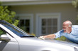 Senior man polishing silver car parked on driveway in front of house, smiling, side view