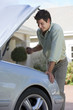 Photo: Man standing beside parked convertible car on driveway, looking at engine, smiling, side view Man standing beside parked convertible car on driveway, looking at engine, smiling, side view