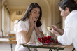 Photo: Couple sitting at pavement café table near colonnade, man proposing to woman, smiling, side view Couple sitting at pavement café table near colonnade, man proposing to woman, smiling, side view