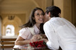 Photo: Couple sitting at pavement café table near colonnade, man kissing woman on cheek, woman holding engagement ring in box, smiling, side view Couple sitting at pavement café table near colonnade, man kissing woman on cheek, woman holding engagement ring in box, smiling, side view