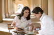 Photo: Couple sitting at pavement café table near colonnade, looking at tourist guide and street map, smiling Couple sitting at pavement café table near colonnade, looking at tourist guide and street map, smiling