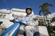 Photo: USA, California, San Diego, Balboa Park, senior man riding on blue motor scooter, smiling, side view, low angle view USA, California, San Diego, Balboa Park, senior man riding on blue motor scooter, smiling, side view, low angle view