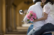 Photo: Couple riding on motor scooter near colonnade, woman holding bouquet of pink flowers, looking over shoulder, smiling, mid-section, rear view Couple riding on motor scooter near colonnade, woman holding bouquet of pink flowers, looking over shoulder, smiling, mid-section, rear view