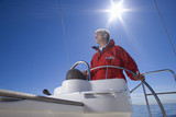 Photo: Man in red jacket standing at helm of sailing boat out at sea, smiling, steering, low angle view (lens flare) Man in red jacket standing at helm of sailing boat out at sea, smiling, steering, low angle view (lens flare)