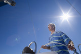 Photo: Man in striped blue polo shirt standing at helm of sailing boat out at sea, steering, low angle view (lens flare) Man in striped blue polo shirt standing at helm of sailing boat out at sea, steering, low angle view (lens flare)