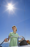 Photo: Woman in green polo shirt standing at helm of sailing boat out at sea, smiling, steering (lens flare, tilt) Woman in green polo shirt standing at helm of sailing boat out at sea, smiling, steering (lens flare, tilt)