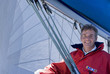 Photo: Man in red jacket sitting on deck of sailing boat below sail, smiling, portrait, low angle view Man in red jacket sitting on deck of sailing boat below sail, smiling, portrait, low angle view