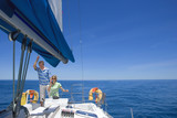 Photo: Couple standing at helm of sailing boat out to sea, holding hands, woman steering, man leaning on sail rigging, smiling Couple standing at helm of sailing boat out to sea, holding hands, woman steering, man leaning on sail rigging, smiling