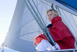 Photo: Woman in red jacket sitting on deck of sailing boat below sail, daydreaming, side view, low angle view Woman in red jacket sitting on deck of sailing boat below sail, daydreaming, side view, low angle view