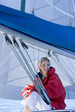 Photo: Woman in red jacket sitting on deck of sailing boat below sail, smiling, side view Woman in red jacket sitting on deck of sailing boat below sail, smiling, side view