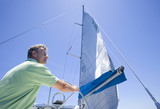 Photo: Man in green polo shirt standing at helm of sailing boat, steering, rear view, low angle view Man in green polo shirt standing at helm of sailing boat, steering, rear view, low angle view