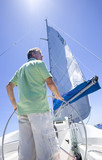 Photo: Man in green polo shirt standing at helm of sailing boat, steering, rear view, low angle view (lens flare) Man in green polo shirt standing at helm of sailing boat, steering, rear view, low angle view (lens flare)