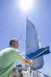 Photo: Man in green polo shirt standing at helm of sailing boat, steering, rear view, low angle view (lens flare) Man in green polo shirt standing at helm of sailing boat, steering, rear view, low angle view (lens flare)