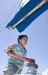 Photo: Boy (8-10) winding rope pulley of boat rigging on deck of sailing boat out at sea, smiling, low angle view Boy (8-10) winding rope pulley of boat rigging on deck of sailing boat out at sea, smiling, low angle view