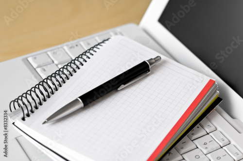 A laptop, a notebook and a pen on a desk. 