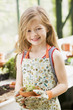Young girl in greenhouse holding potted plant smiling
