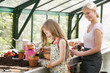 Young girl and woman in greenhouse putting soil in pots smiling
