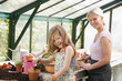 Young girl and woman in greenhouse putting soil in pots smiling