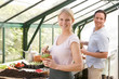 Couple in greenhouse raking soil in pots smiling