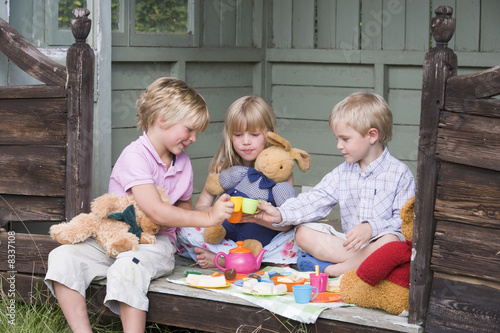 Three young children in shed playing tea and smiling Three young children in shed playing tea and smiling