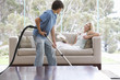 A young boy vacuuming whilst his mother relaxes