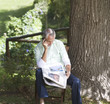 Man with a newspaper and mobile phone sitting next to a tree
