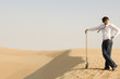 A young man standing in the desert with a spade