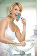 Woman in bathroom brushing teeth smiling