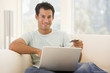 Photo: Man in living room using laptop and holding credit card smiling Man in living room using laptop and holding credit card smiling