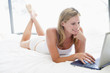 Woman lying in bed with laptop smiling