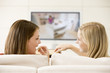 Two women in living room watching television eating chocolates s