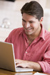 Man in kitchen using laptop smiling