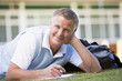 A man writing notes while lying on a campus lawn