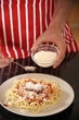 Man sprinkling cheese on spaghetti