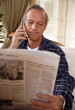 Mature man reading newspaper and talking on cell phone