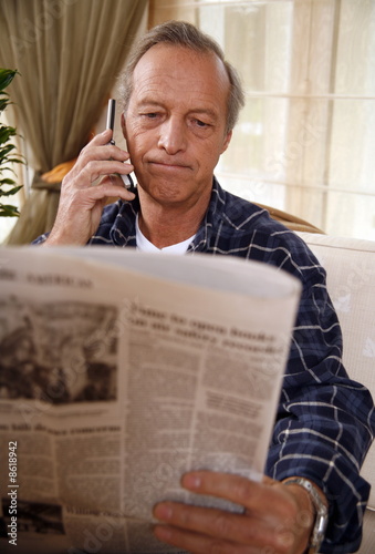 Photo: Mature man reading newspaper and talking on cell phone Mature man reading newspaper and talking on cell phone