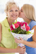 Granddaughter kissing grandmother on cheek holding flowers and s