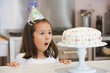 Photo: Young girl wearing party hat at kitchen counter looking at cake Young girl wearing party hat at kitchen counter looking at cake