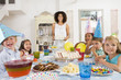 Photo: Young children at party sitting at table with mother carrying ca Young children at party sitting at table with mother carrying ca