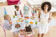 Young children at party sitting at table with mother carrying ca