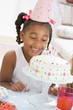 Young girl wearing party hat looking at cake smiling
