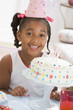 Young girl wearing party hat with cake in front of her smiling