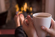 Foto: Feet warming at a fireplace with hands holding coffee Feet warming at a fireplace with hands holding coffee