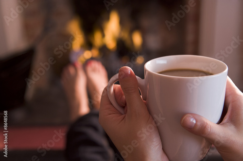Photo: Feet warming at a fireplace with hands holding coffee Feet warming at a fireplace with hands holding coffee